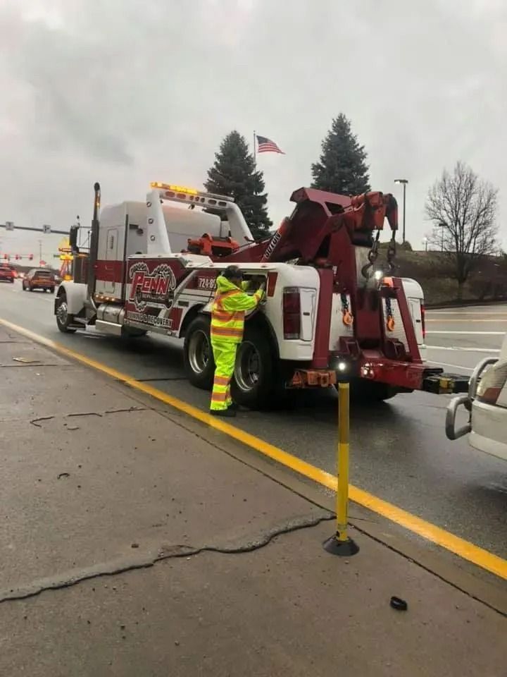 Tow truck operator in reflective vest attaching a car on a rainy road.