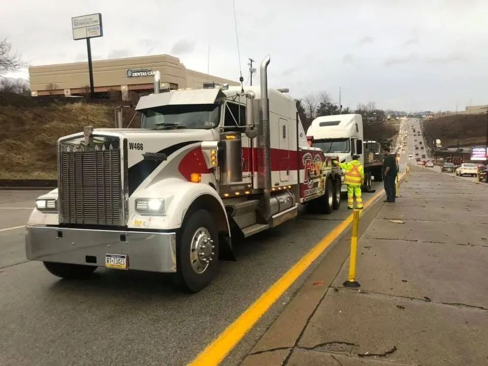 Tow truck hauling another truck on a road. Worker in reflective vest directs traffic.