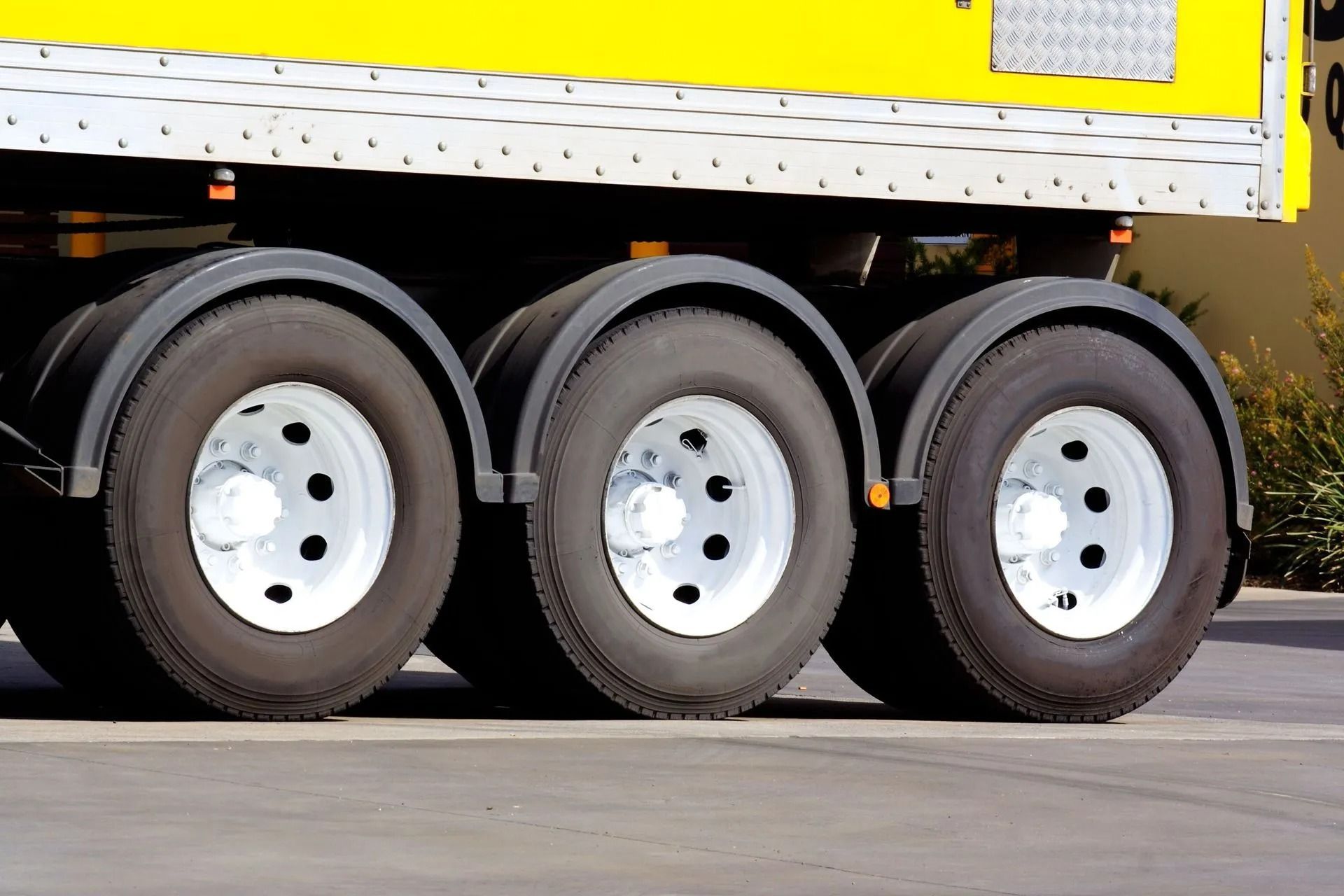 Three truck tires with white rims and black fenders, attached to a yellow trailer.