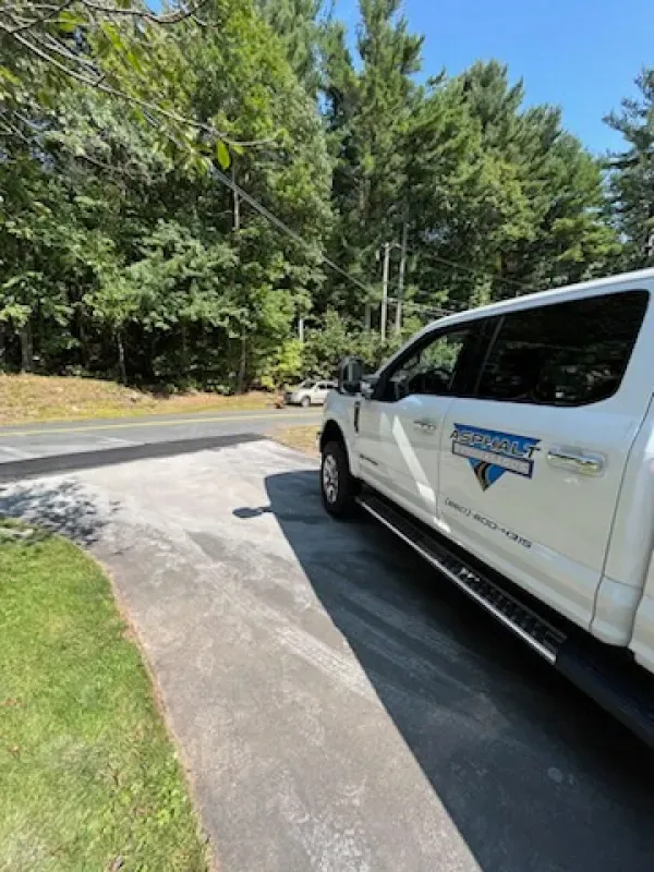 A white truck is parked in a driveway next to a forest