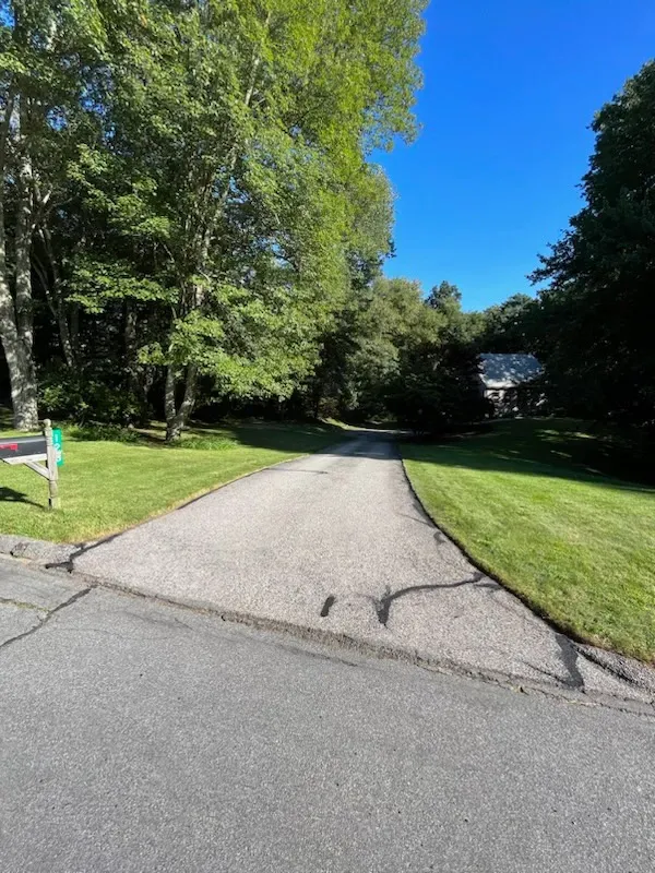 A driveway leading to a house surrounded by trees and grass