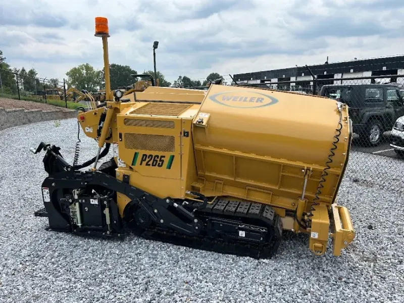 A yellow asphalt paving machine is parked in a gravel lot