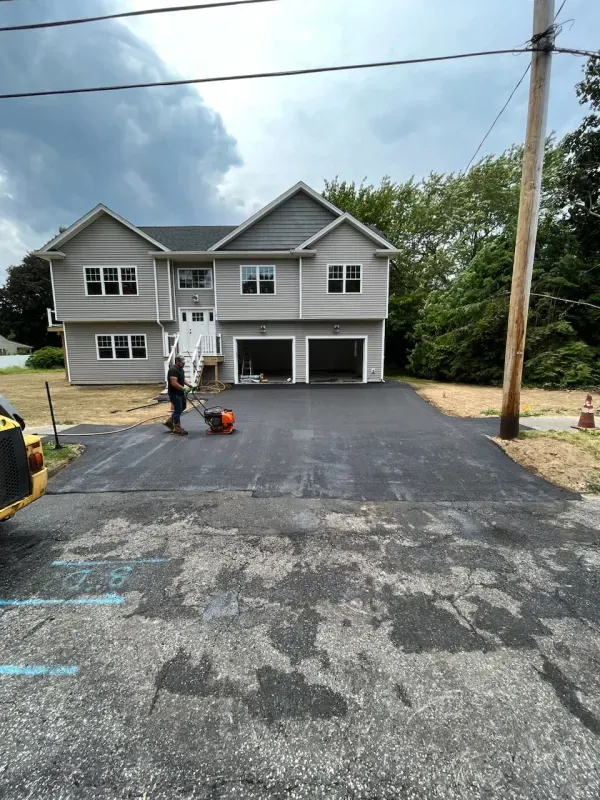 A man is working on a driveway in front of a large house