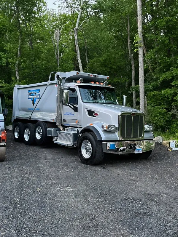 A dump truck is parked in a gravel lot in the woods