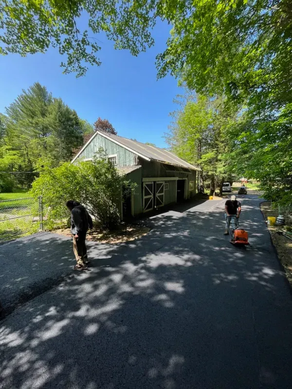 A group of people are working on a driveway in front of a house