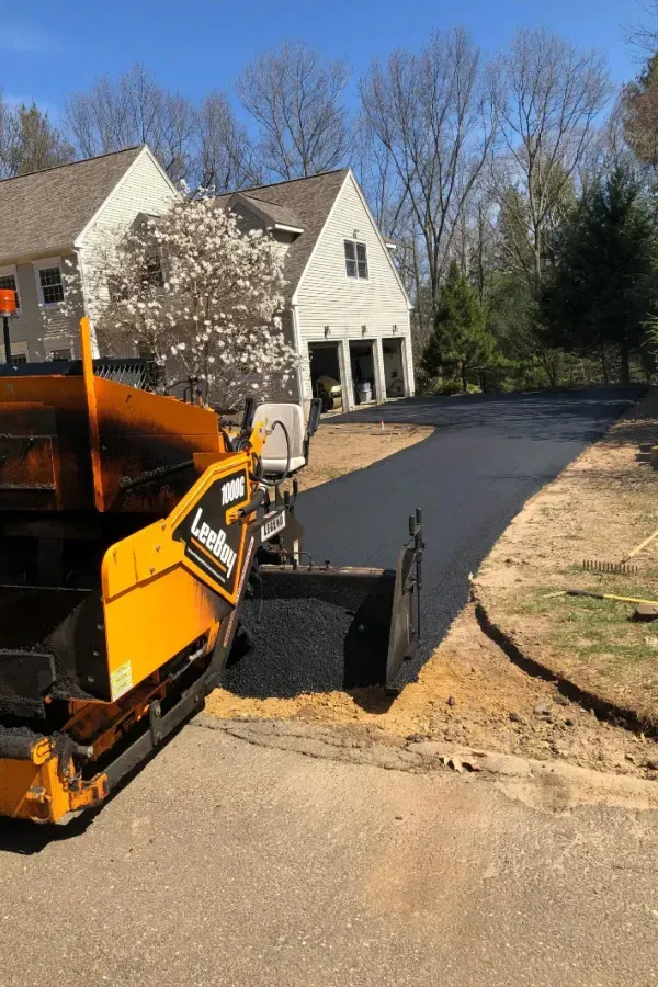 A yellow tractor is paving a driveway in front of a house