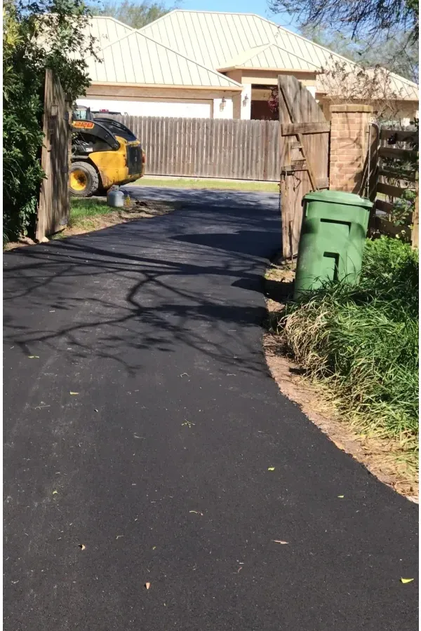 A green trash can is on the side of a road next to a house