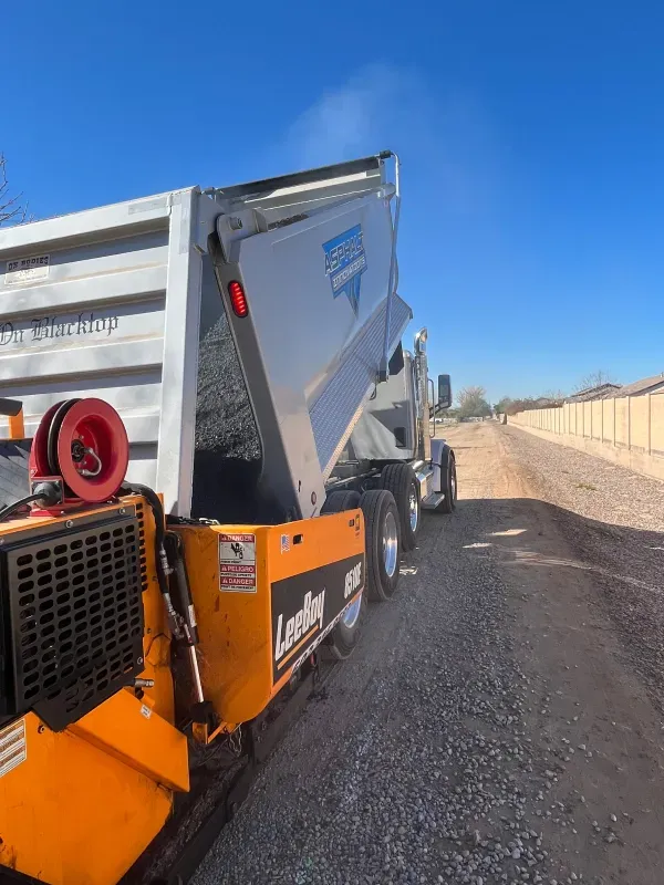 A dump truck is being loaded with gravel on a dirt road