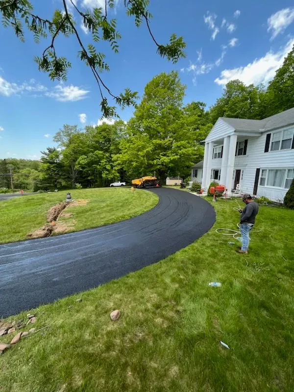 A man is standing next to a curved driveway in front of a large house