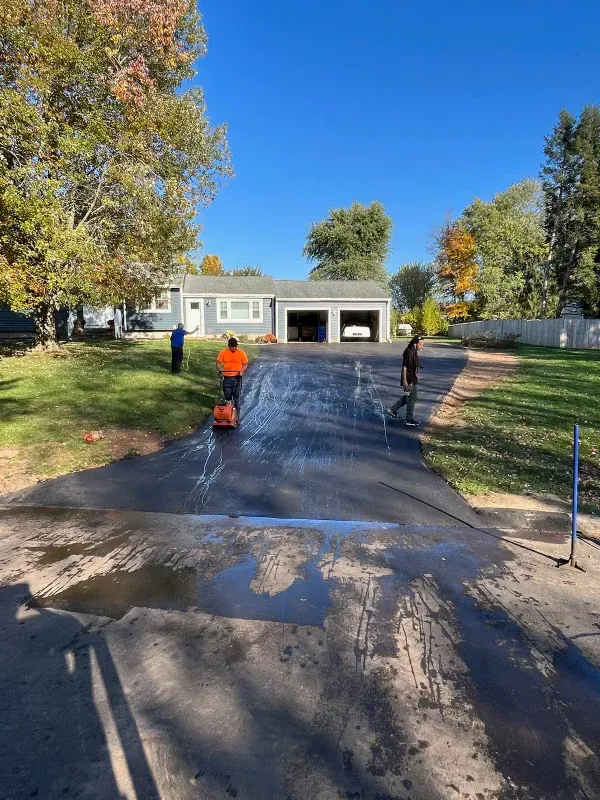 A couple of men are cleaning a driveway in front of a house