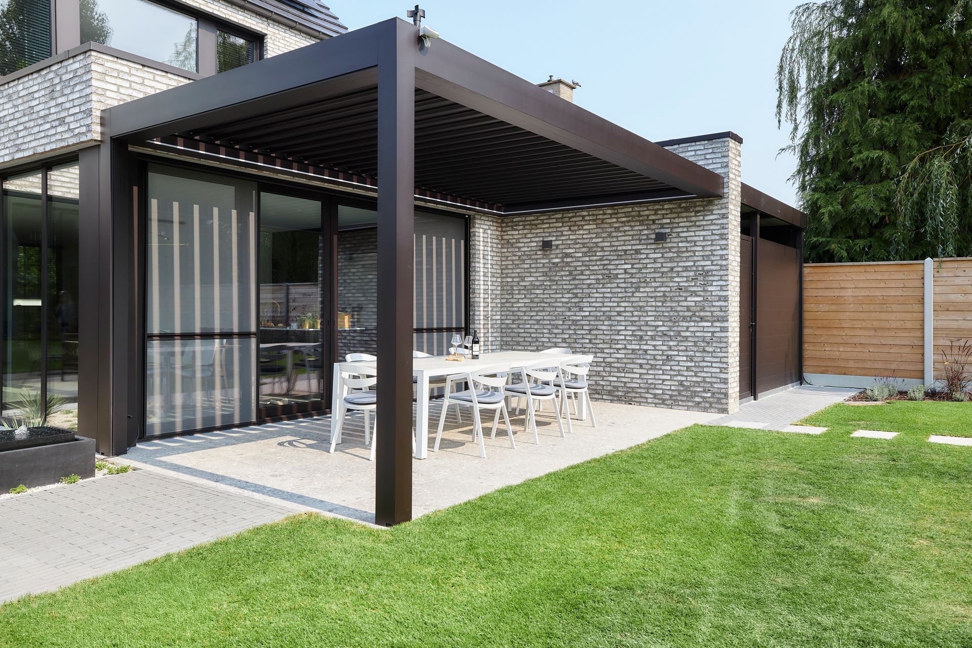 A patio with a table and chairs under a pergola in front of a house.