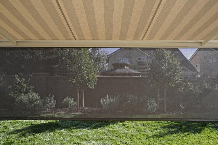 a striped awning is covering a lush green yard with a house in the background