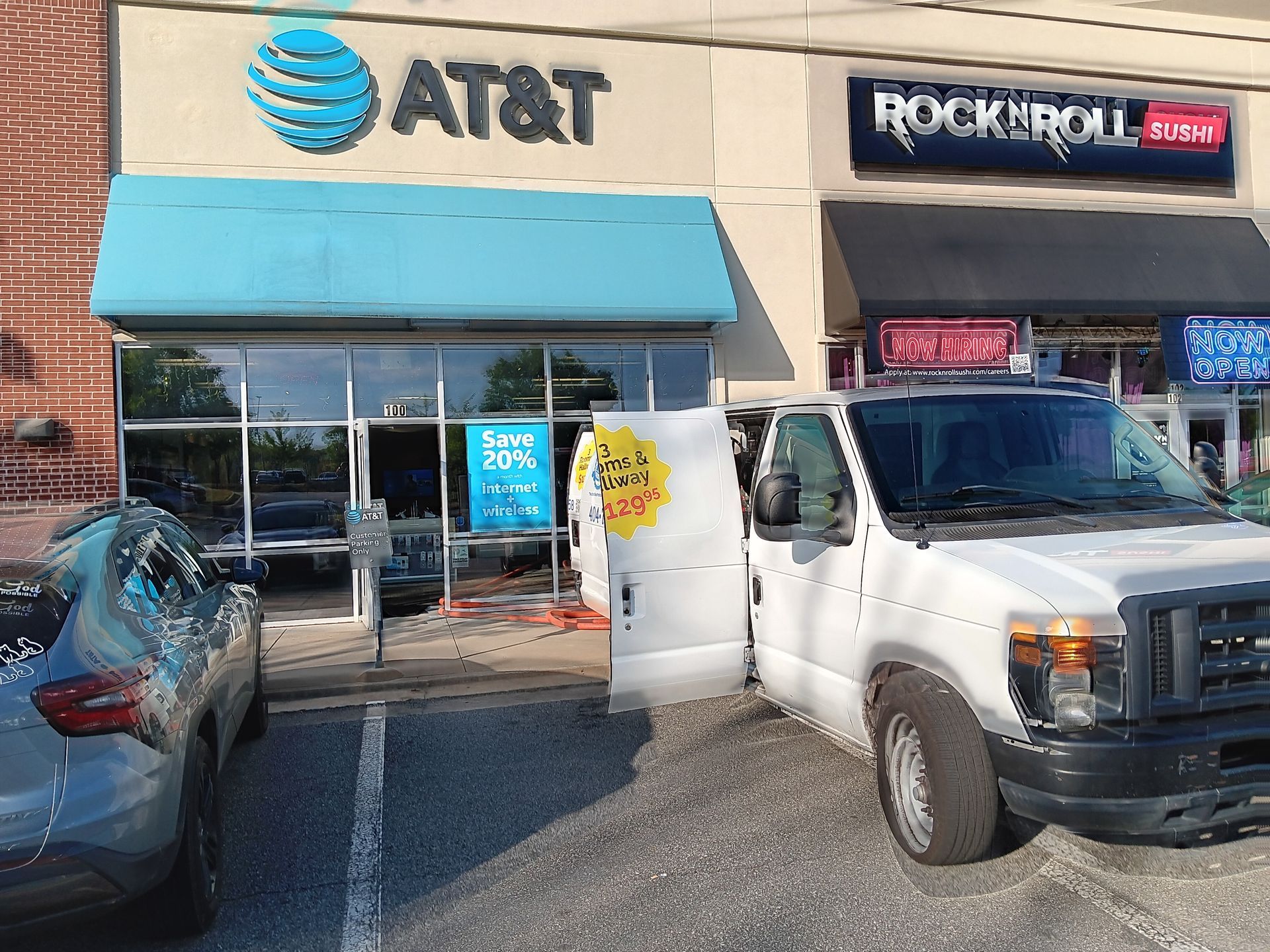 White van parked in front of an AT&T store; a car is parked next to the van. Rock 'n' Roll store next door.