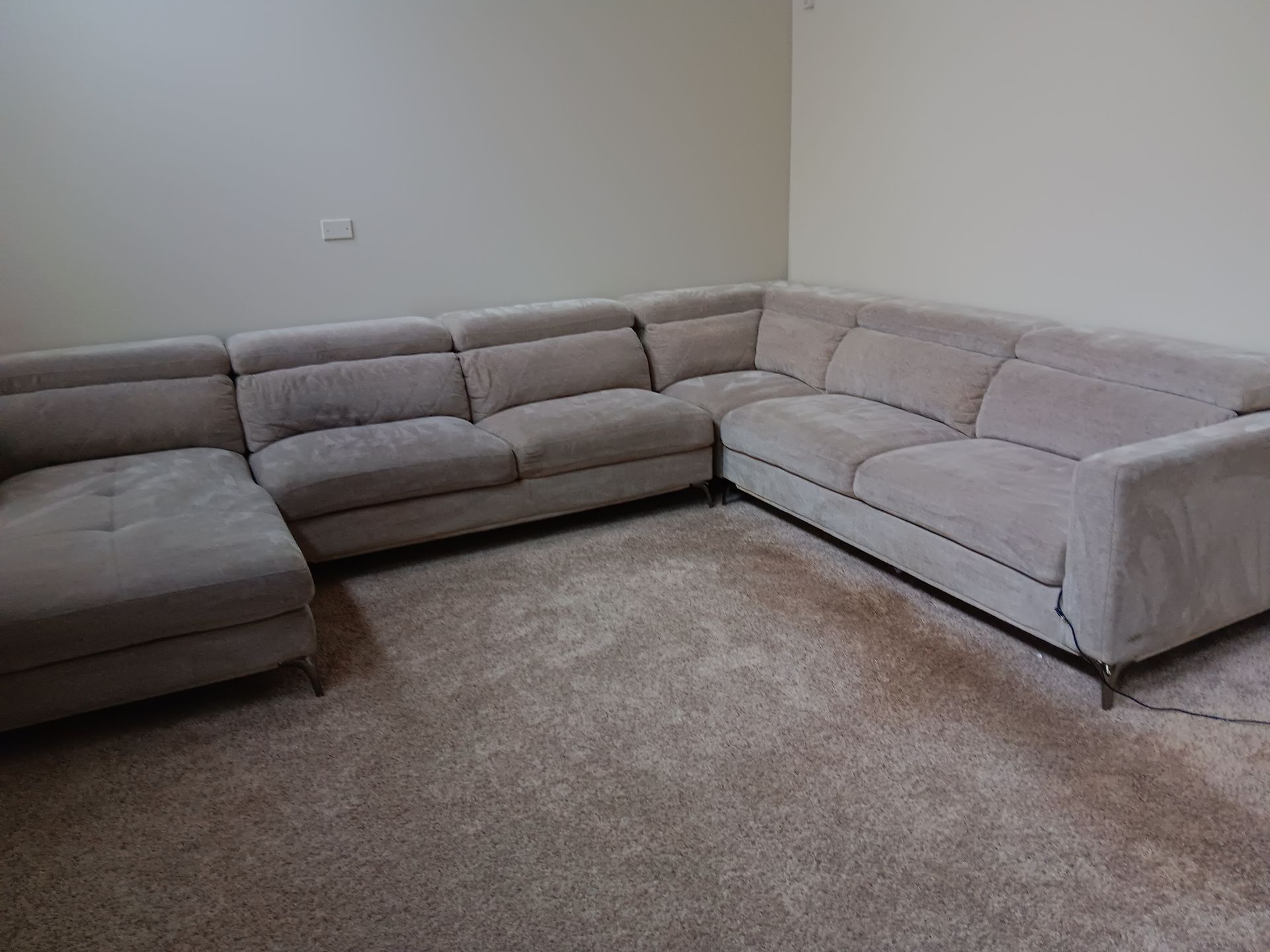 Light grey sectional sofa on tan carpet in a room with light beige walls.