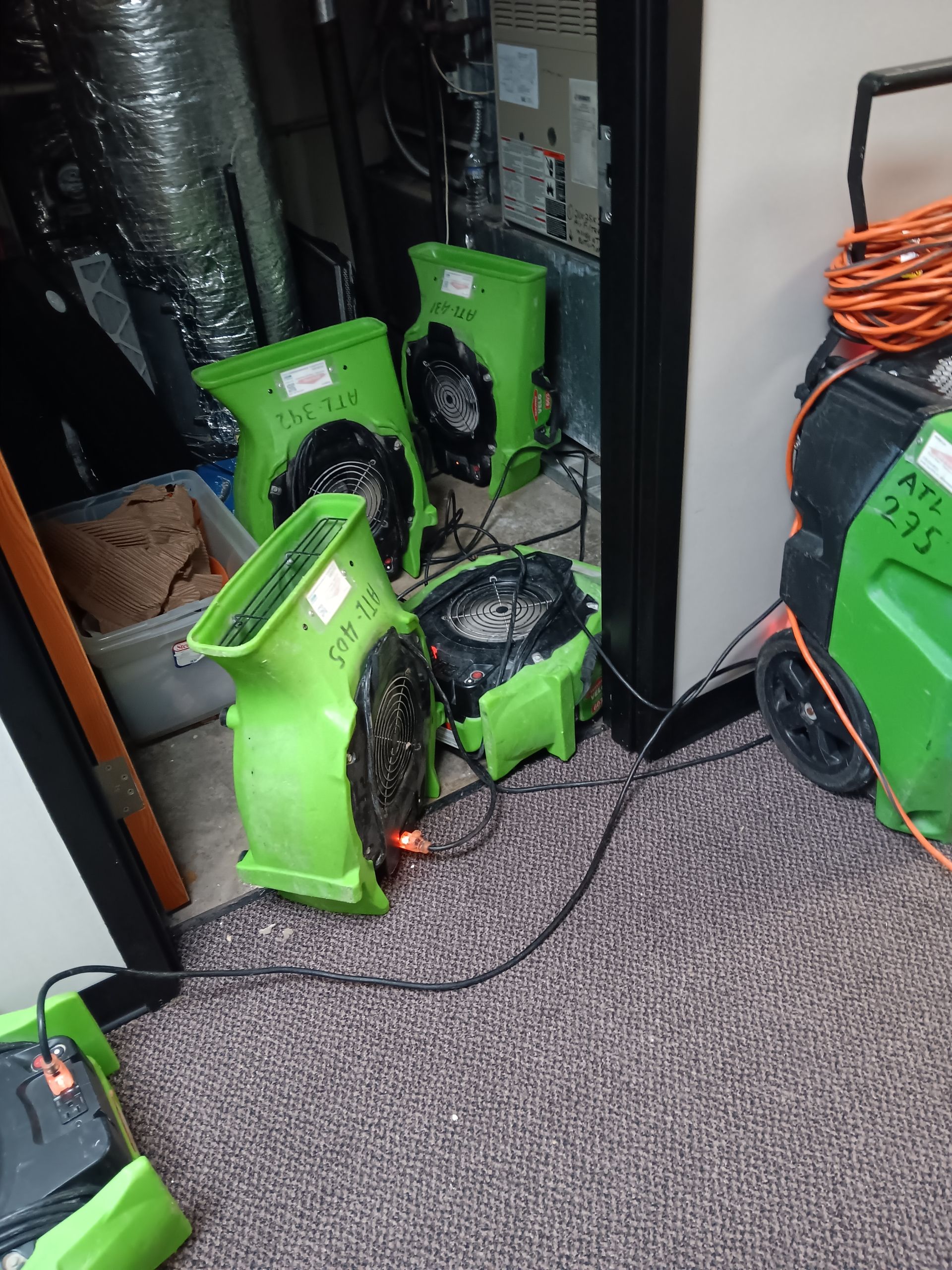 Green fans drying a room with water damage. Carpet, air vent, and equipment visible.