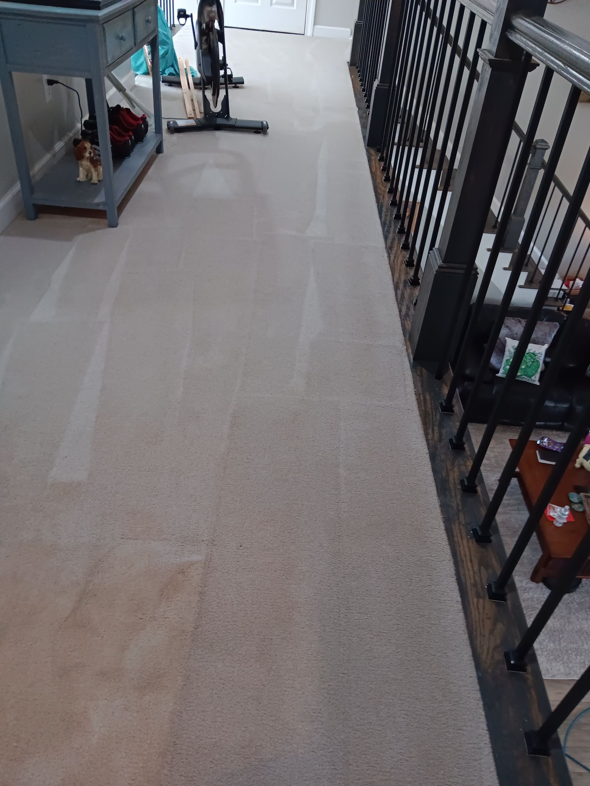 Beige carpeted hallway with a railing on the right, and a blue table on the left.
