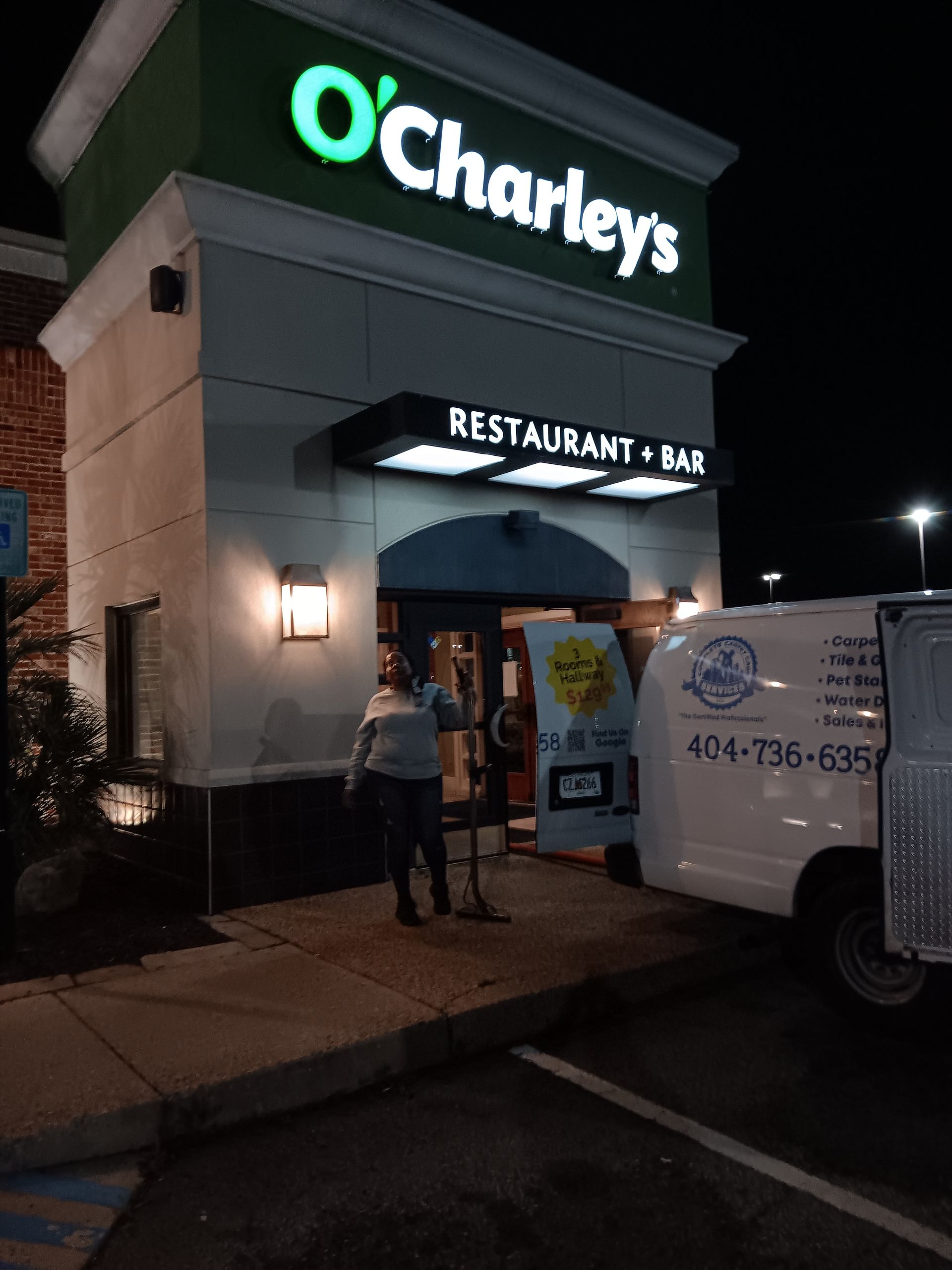 Person standing at entrance of O'Charley's restaurant next to a white van.