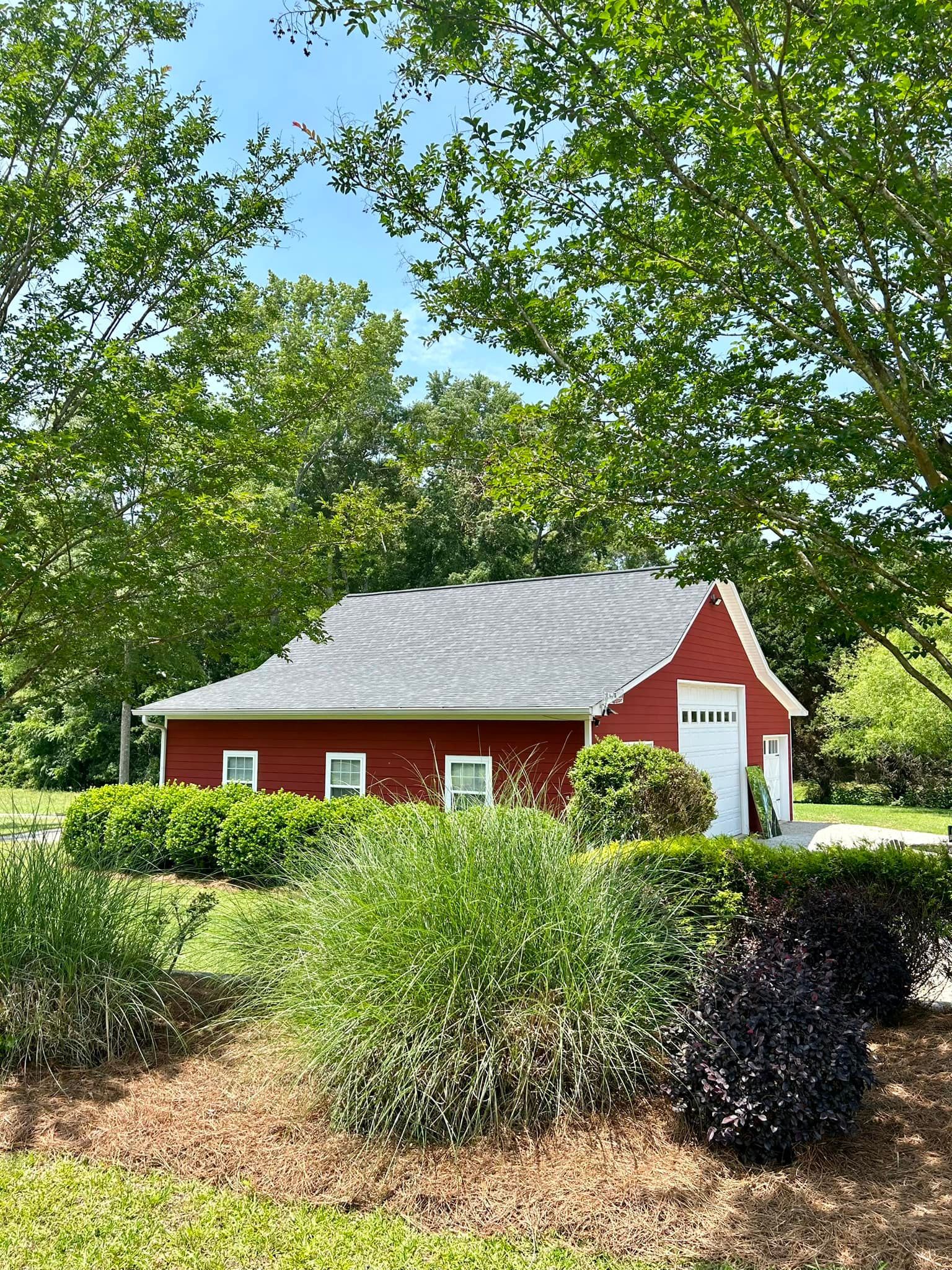 A red barn with a white garage door is surrounded by trees and bushes.