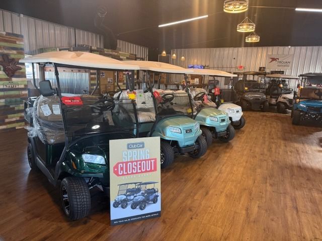Golf carts displayed in a showroom, with a “CLOSED OUT” sale sign in front