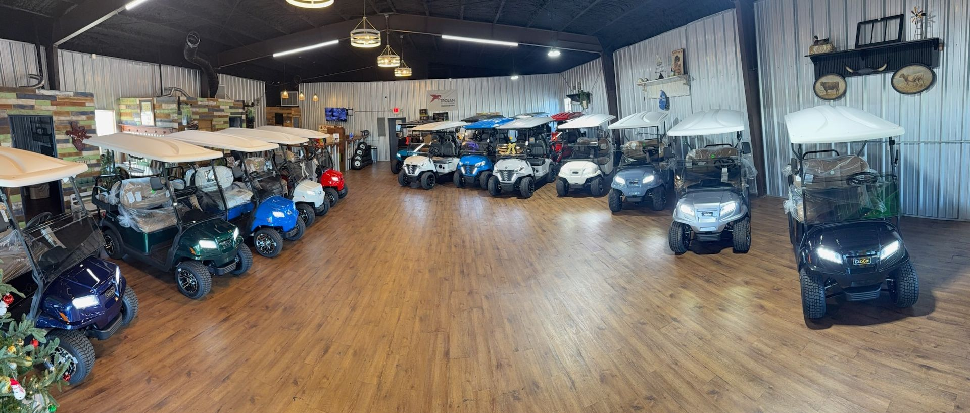 Wide indoor warehouse with rows of parked golf carts and utility vehicles on a wood floor