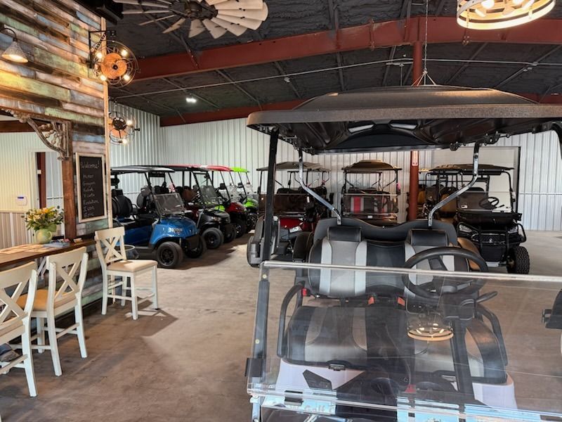 Indoor showroom with several golf carts parked under hanging lights and ceiling fans