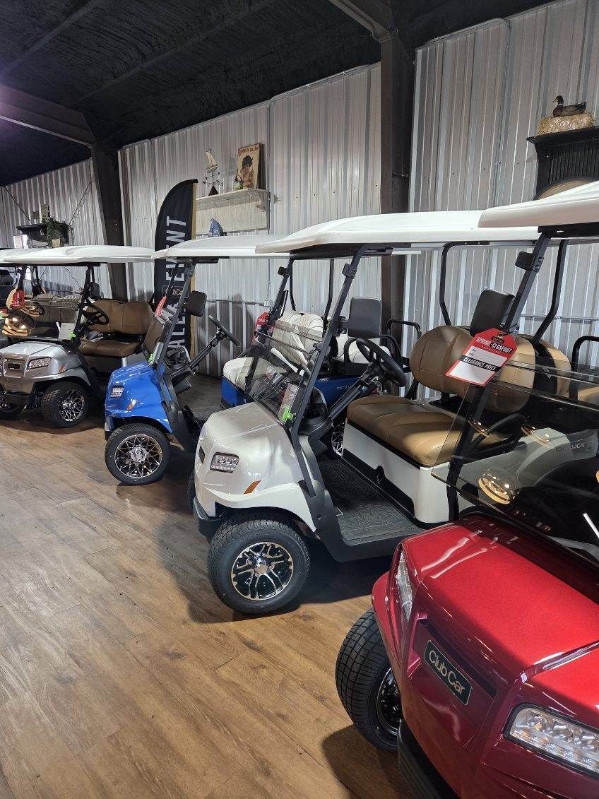 Indoor showroom with several golf carts parked in a row, including white, blue, and red carts.