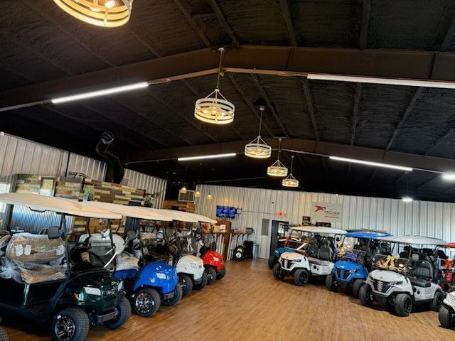 Indoor showroom with rows of golf carts and utility vehicles under hanging lights