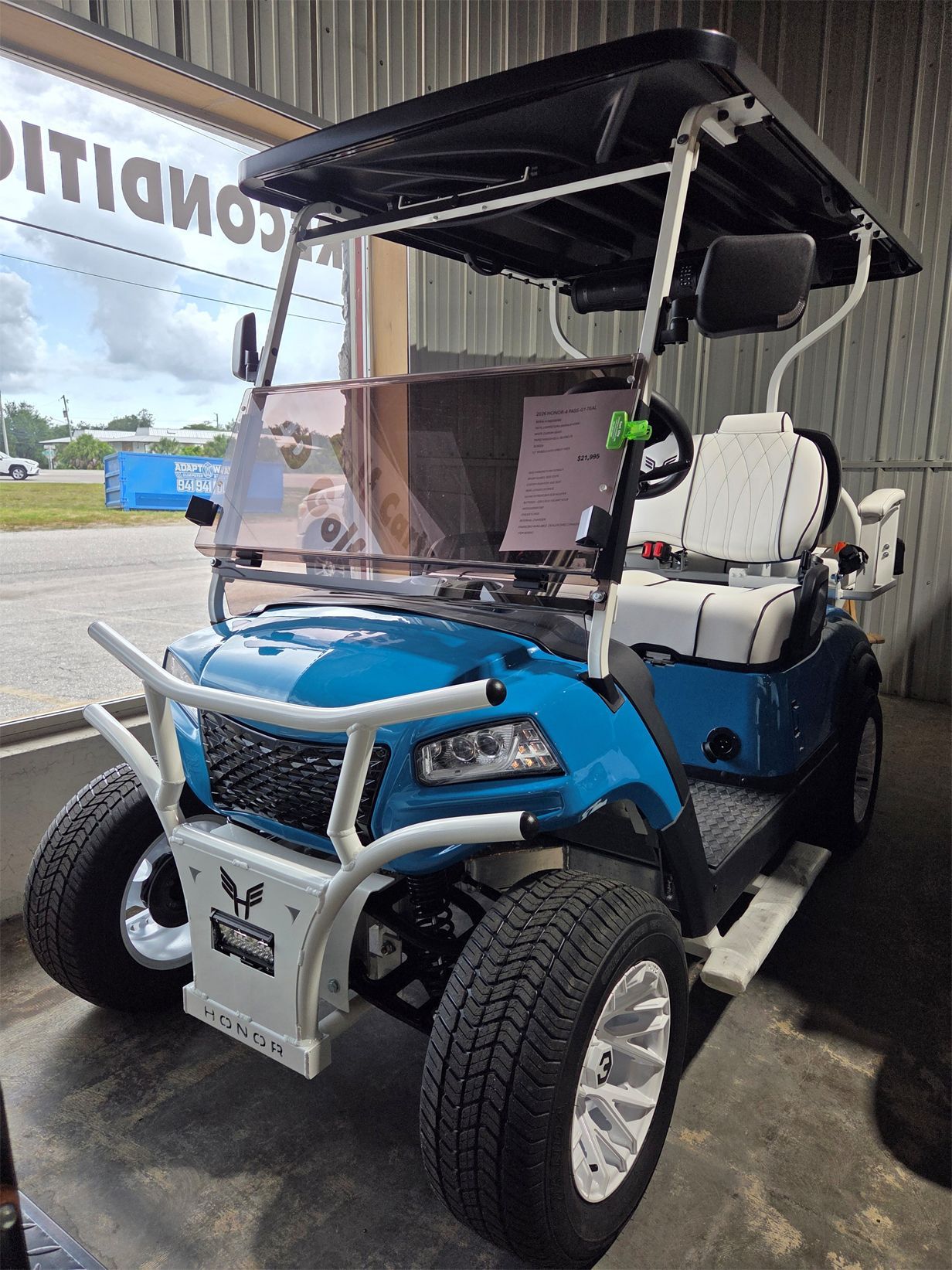 Blue golf cart with white canopy and roll cage parked indoors on a showroom floor