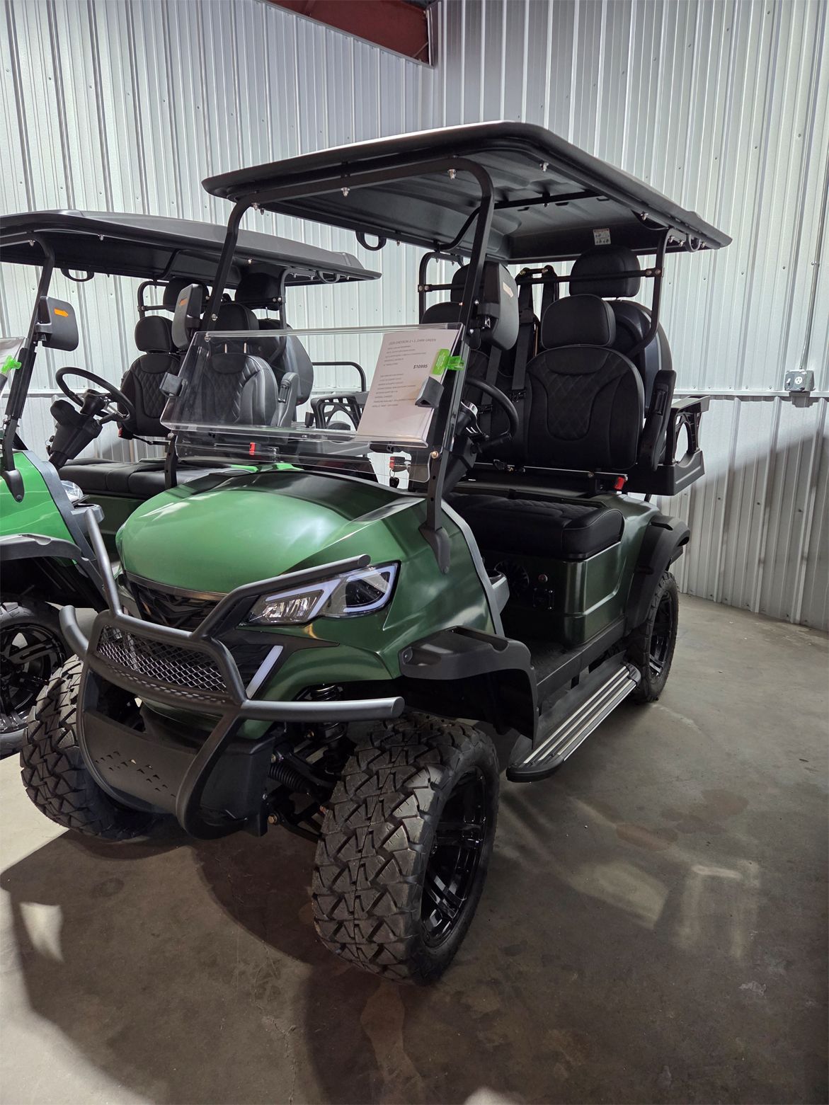 Green off-road golf cart with roof parked indoors on a concrete floor.