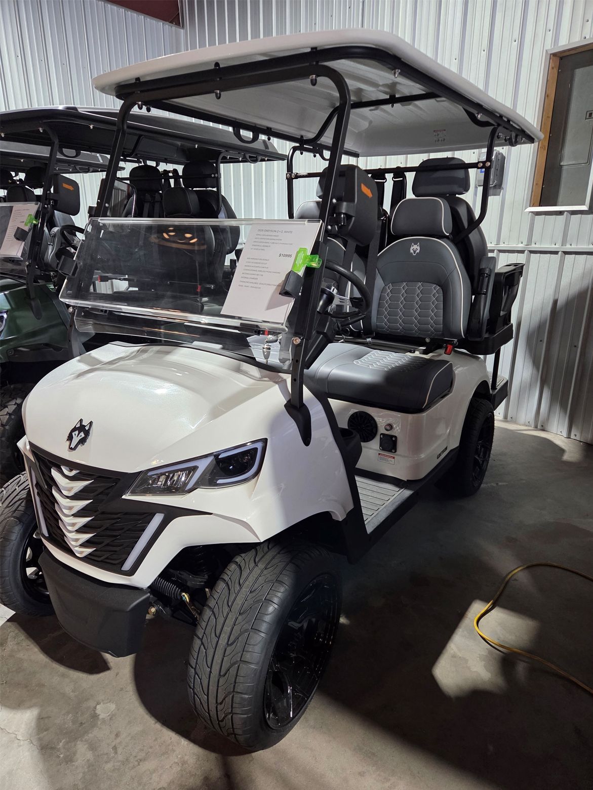 White off-road utility cart with roll cage and windshield, parked indoors on a concrete floor.