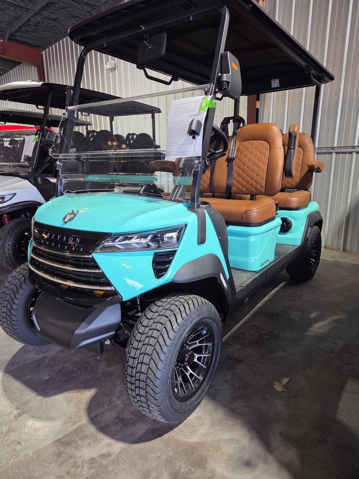 Turquoise golf cart with tan seats and black roof parked indoors under a canopy