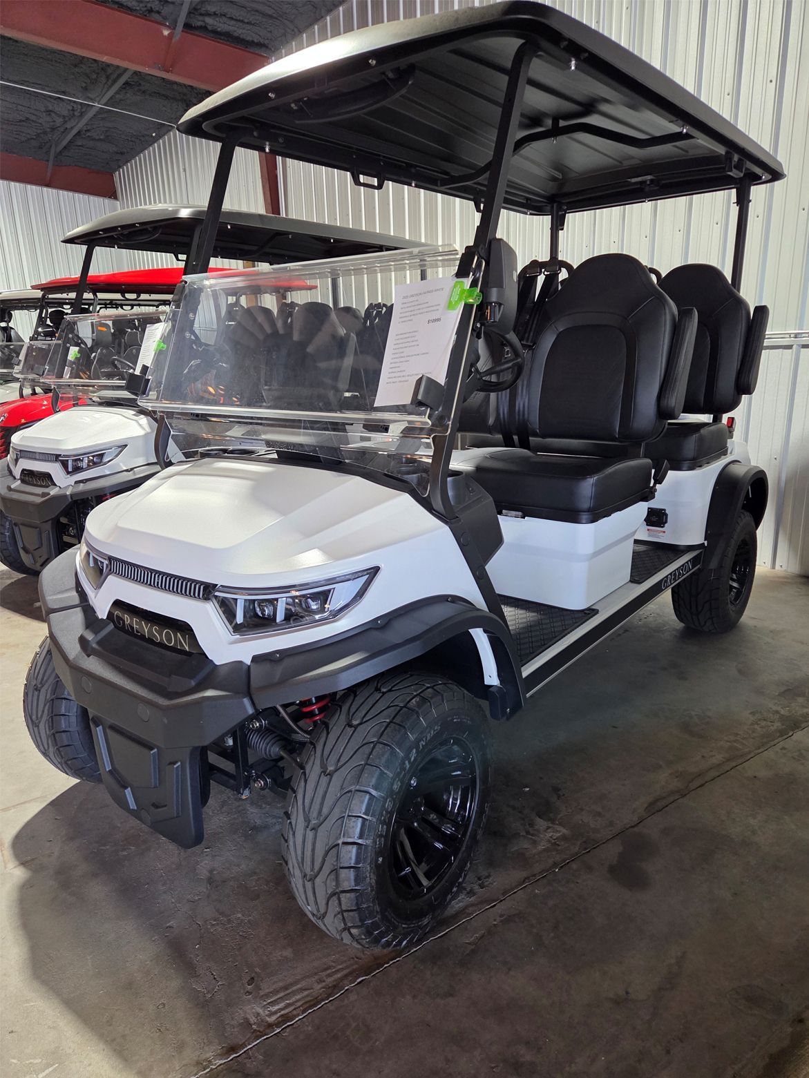 White and black four-seat golf cart with roof and windshield, parked indoors on a showroom floor