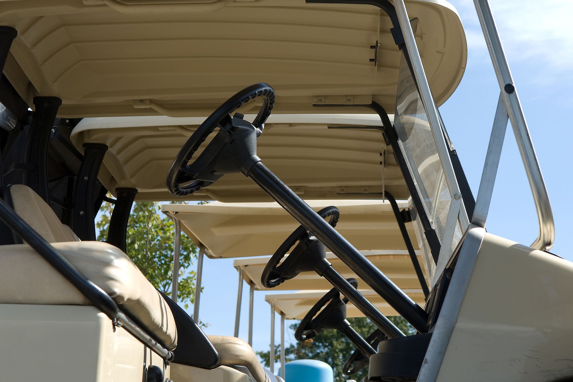 Interior of a beige golf cart with steering wheel and canopy, parked outdoors under a blue sky