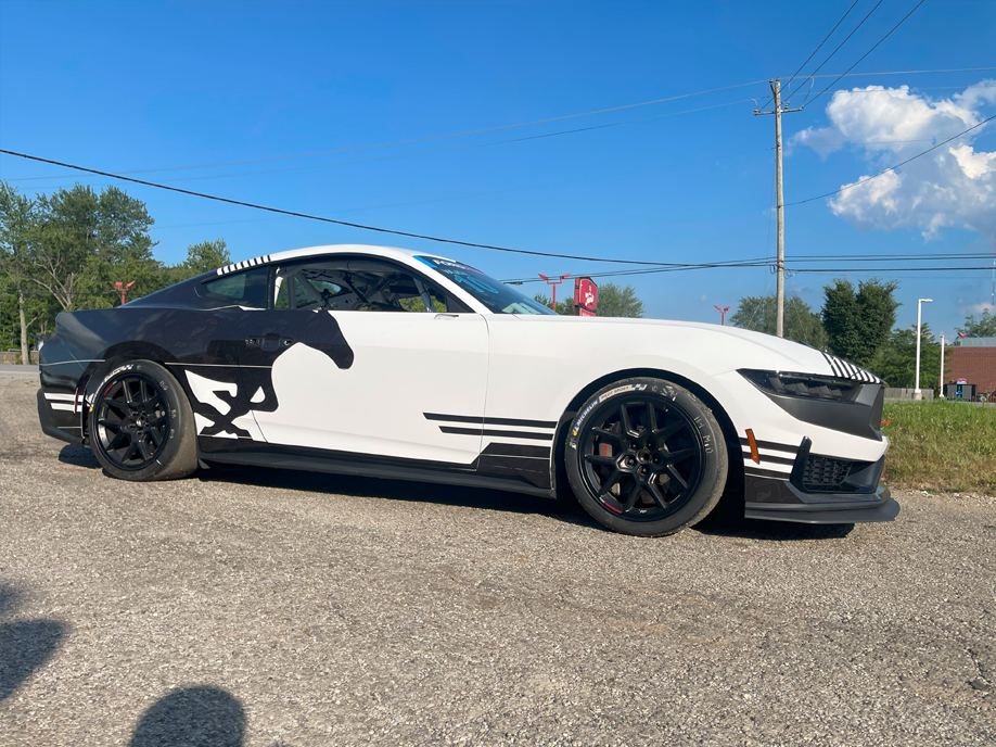 A white mustang with a horse on the side is parked on the side of the road.