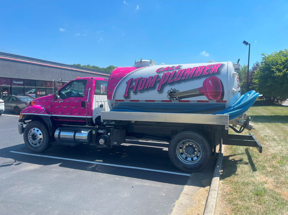 A pink and white vacuum truck is parked in a parking lot.