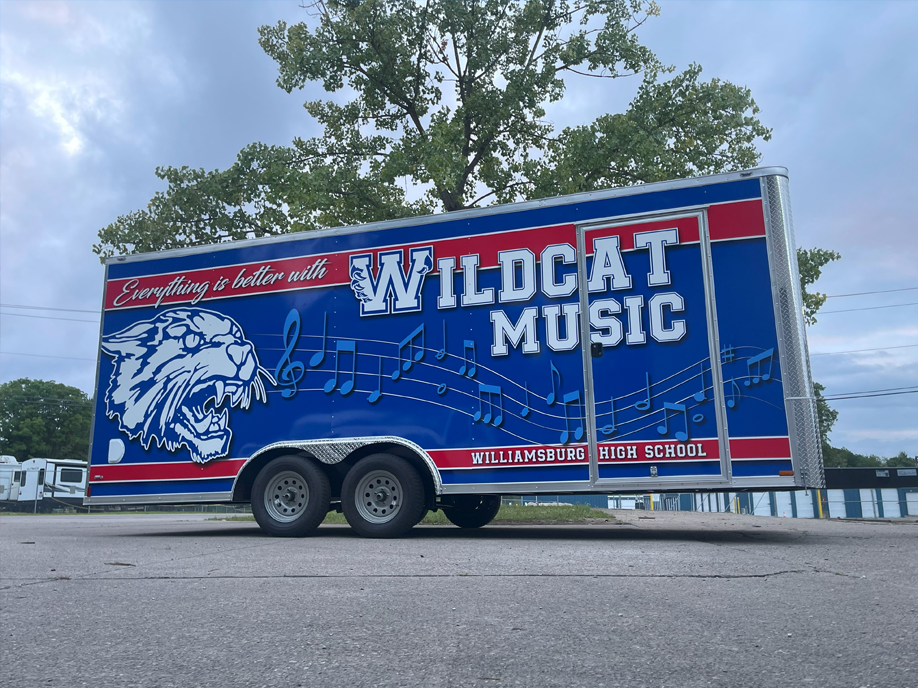 A blue and red trailer for Wildcat Music is parked on the side of the road.