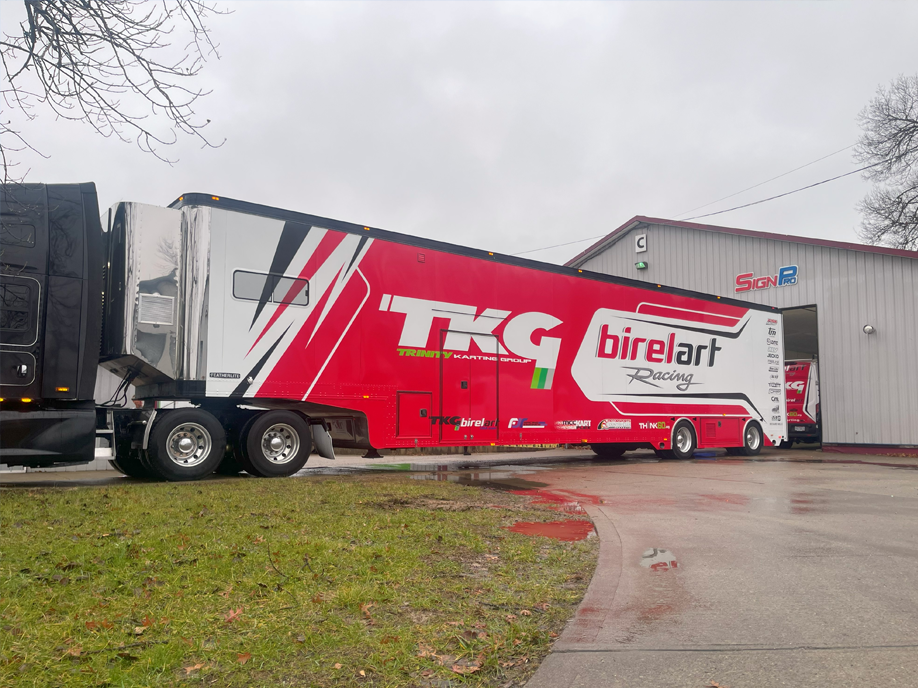 A red trailer with the word TKG on it is parked in front of a building.
