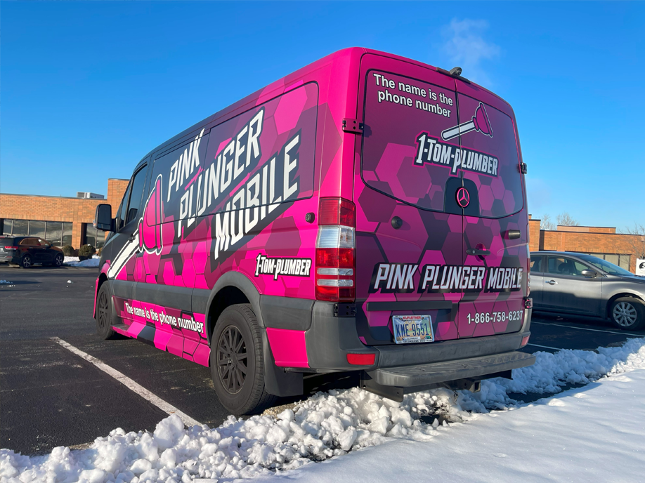 A Pink Plumber Mobile van is parked in a snowy parking lot.