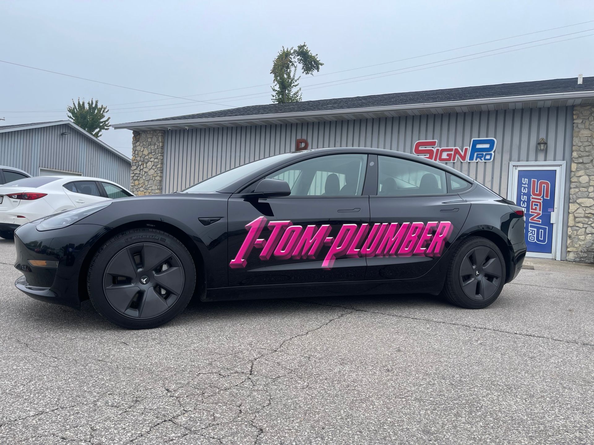 A black tesla model 3 is parked in front of a building.