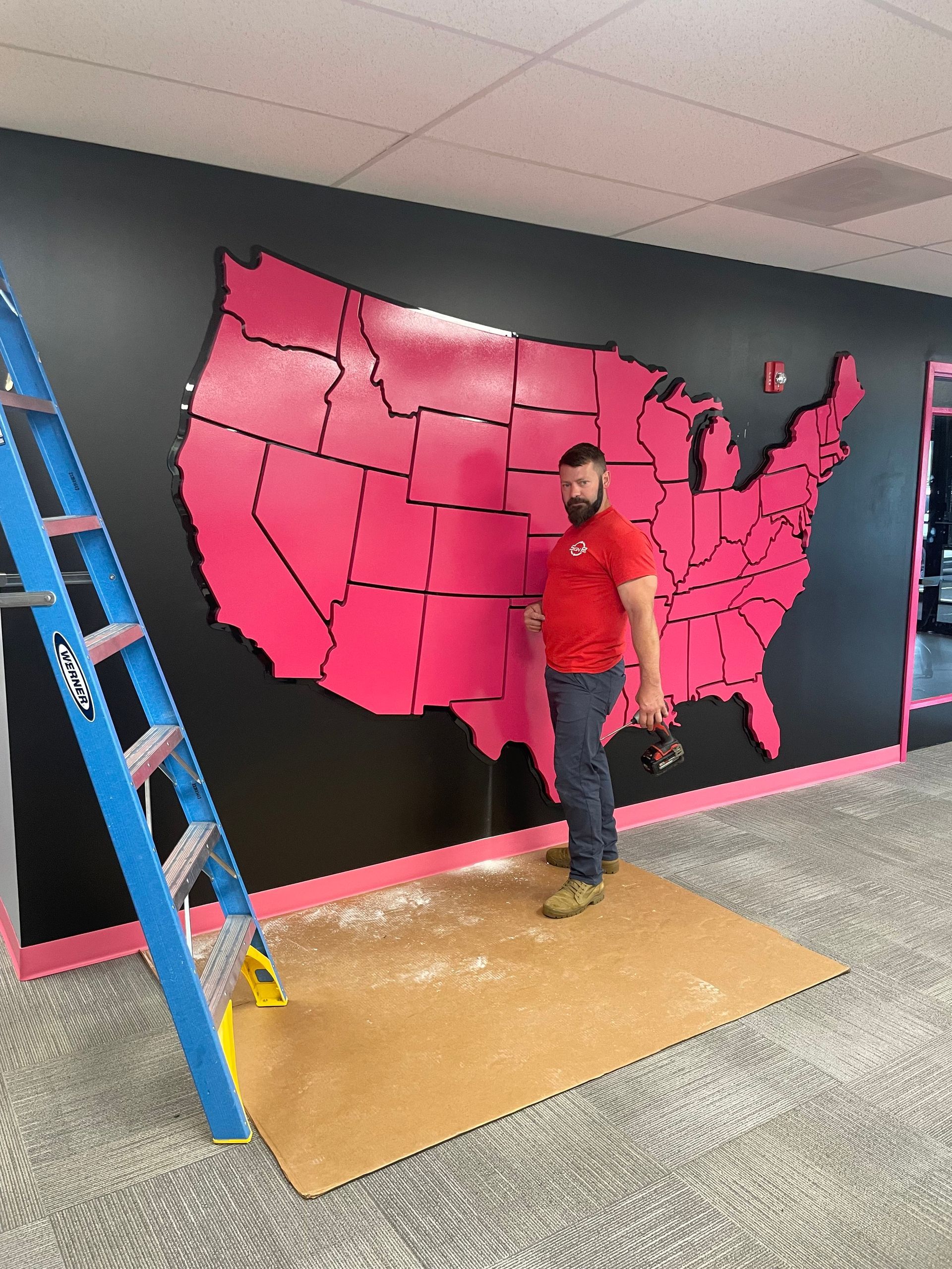 A man is standing in front of a large pink map of the united states.