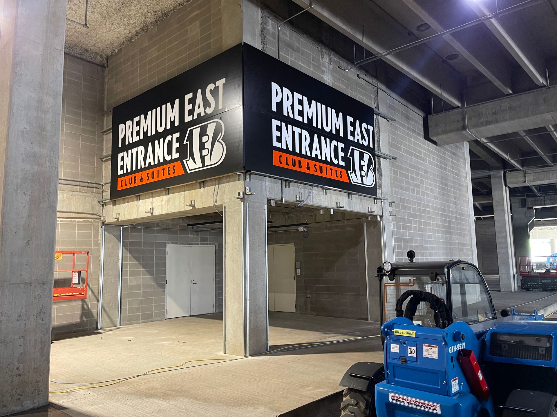 A blue forklift is parked in front of a sign that says premium east entrance