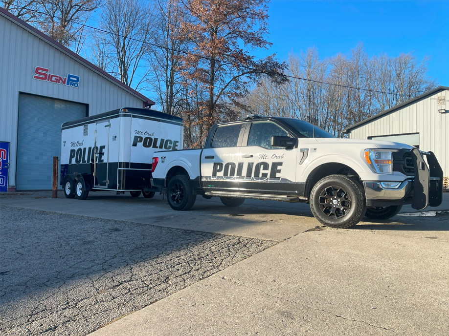 A police truck with a trailer attached to it is parked in front of a building.