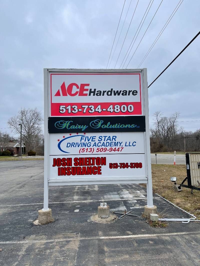 A sign for ace hardware is sitting in a parking lot.