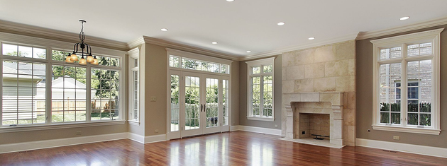 Bright empty living room with hardwood floors, large windows, and a stone fireplace