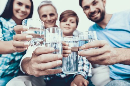 Family smiling in their kitchen with a glass of clean water, highlighting the benefits of whole home