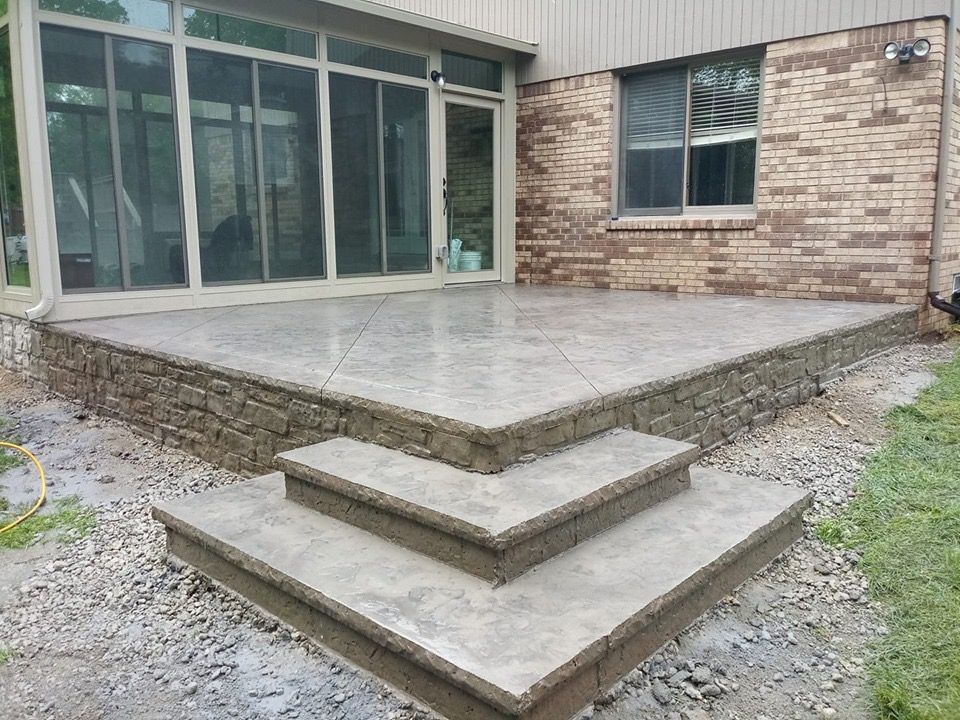 Concrete patio with two stepped platforms beside a house’s glass sliding doors and brick wall.