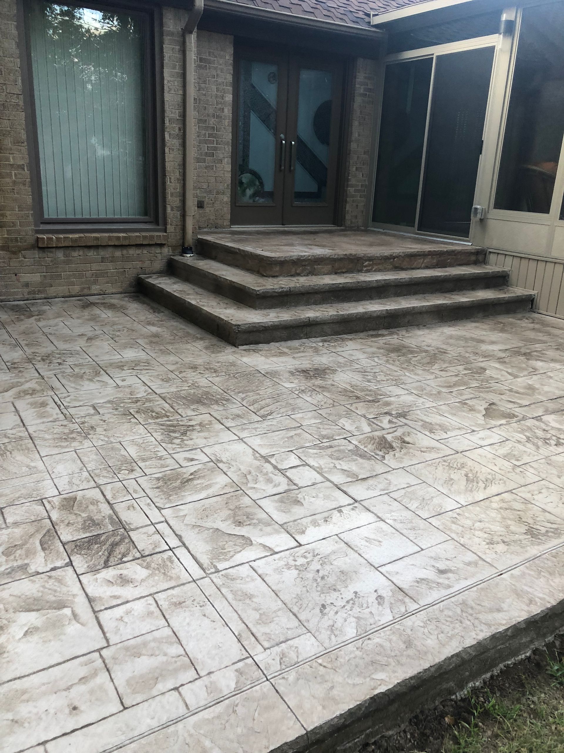 Outdoor tiled patio with three steps leading to a front door and windows of a brick house