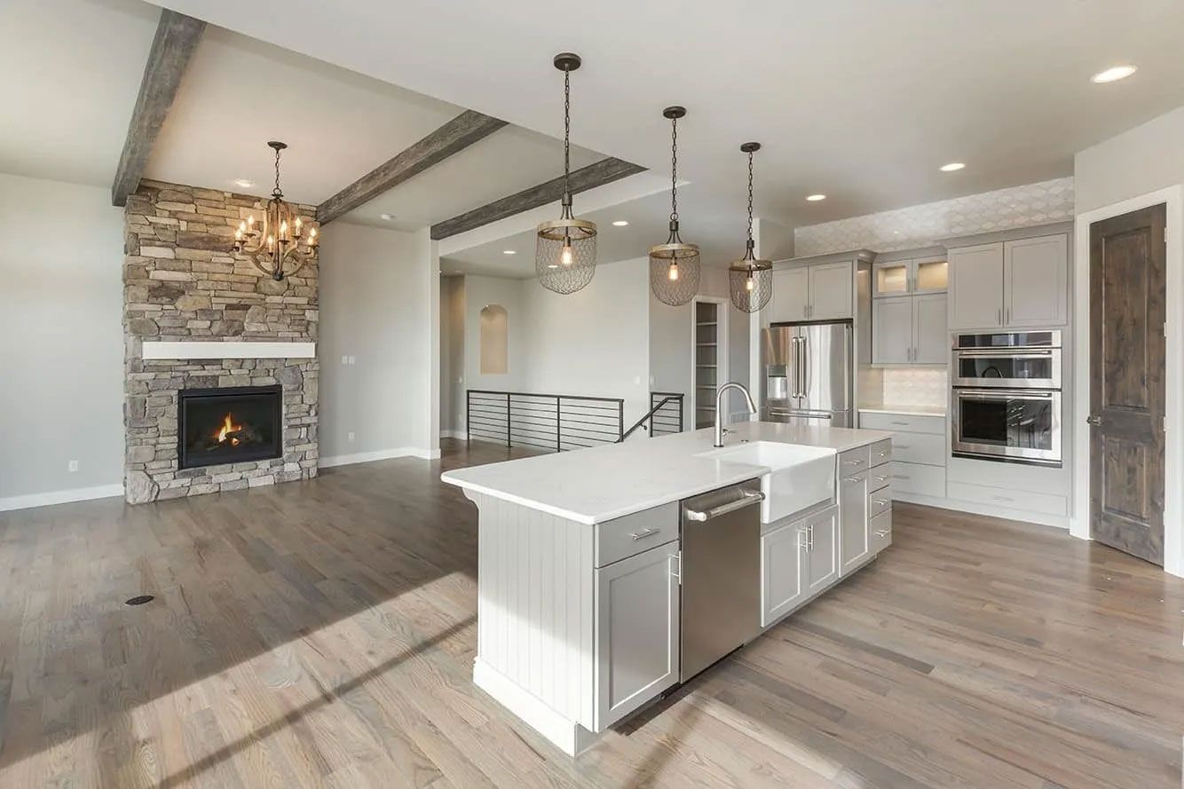Modern open-concept kitchen and living area with a stone fireplace, gray island, and wood flooring.