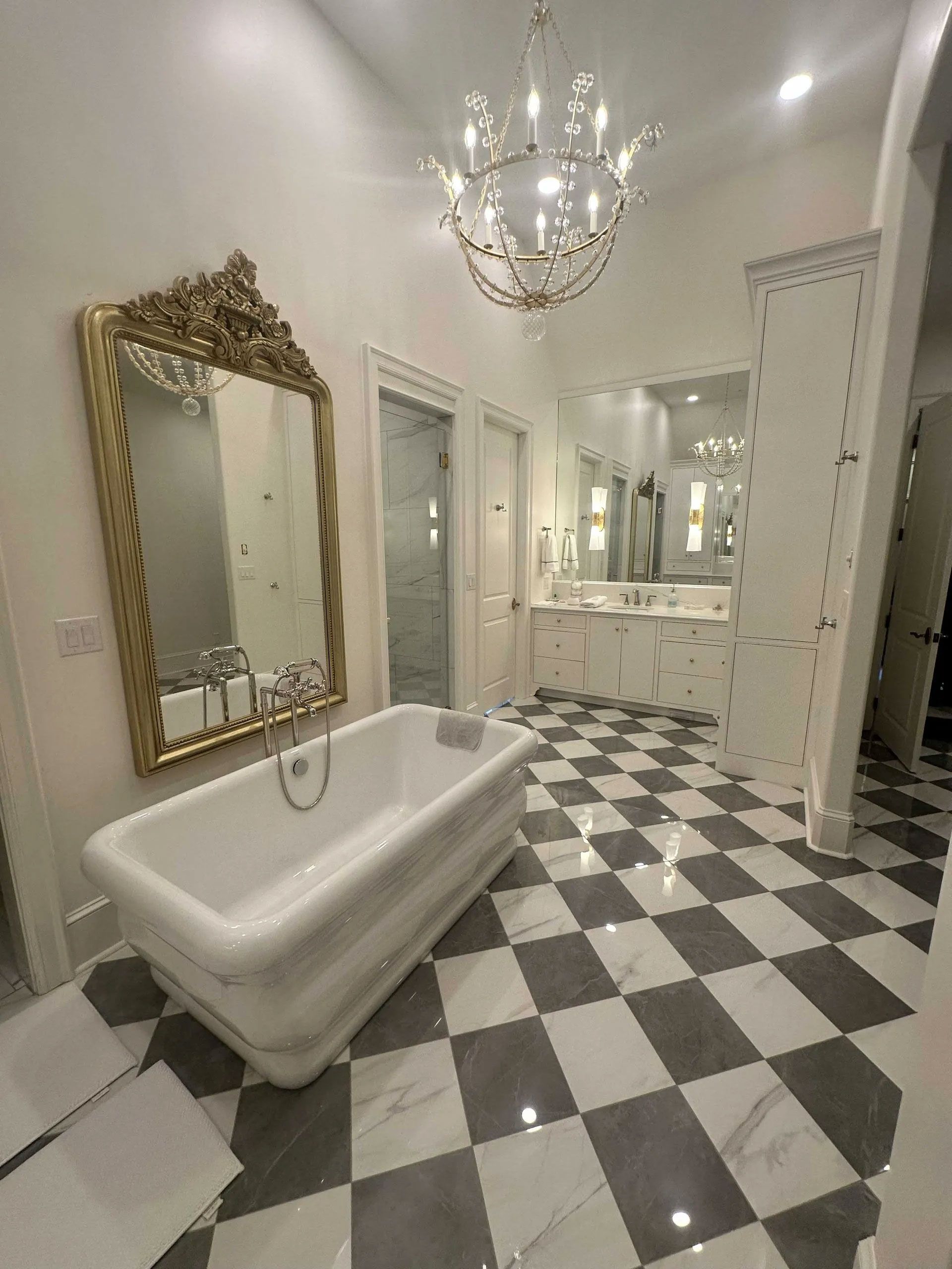 A luxurious bathroom with a white freestanding tub, gold-framed mirror, and checkered black and white marble tile floors.
