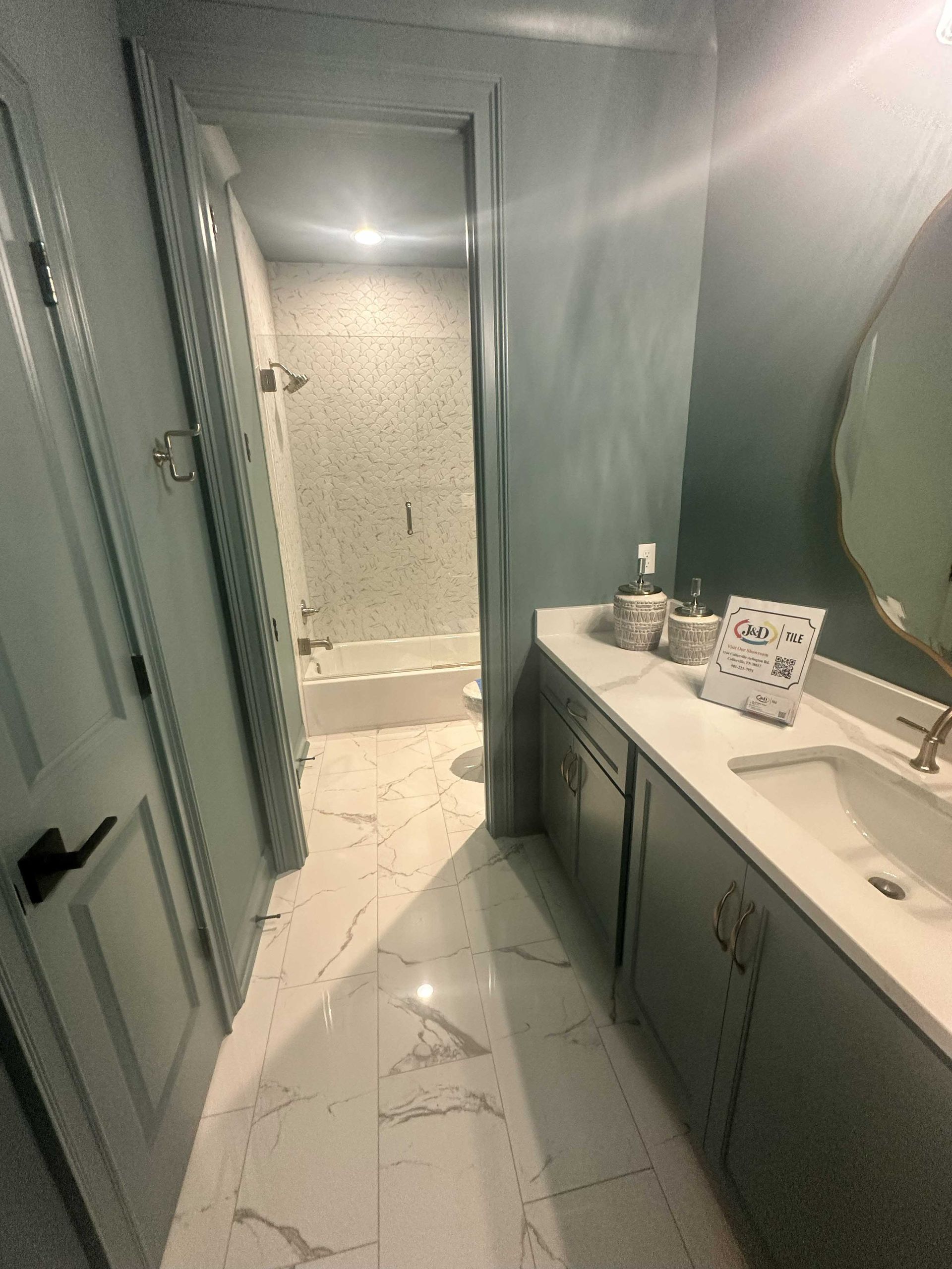 Bathroom with blue-green walls, white marble floors, a vanity, and a shower visible through an open door.